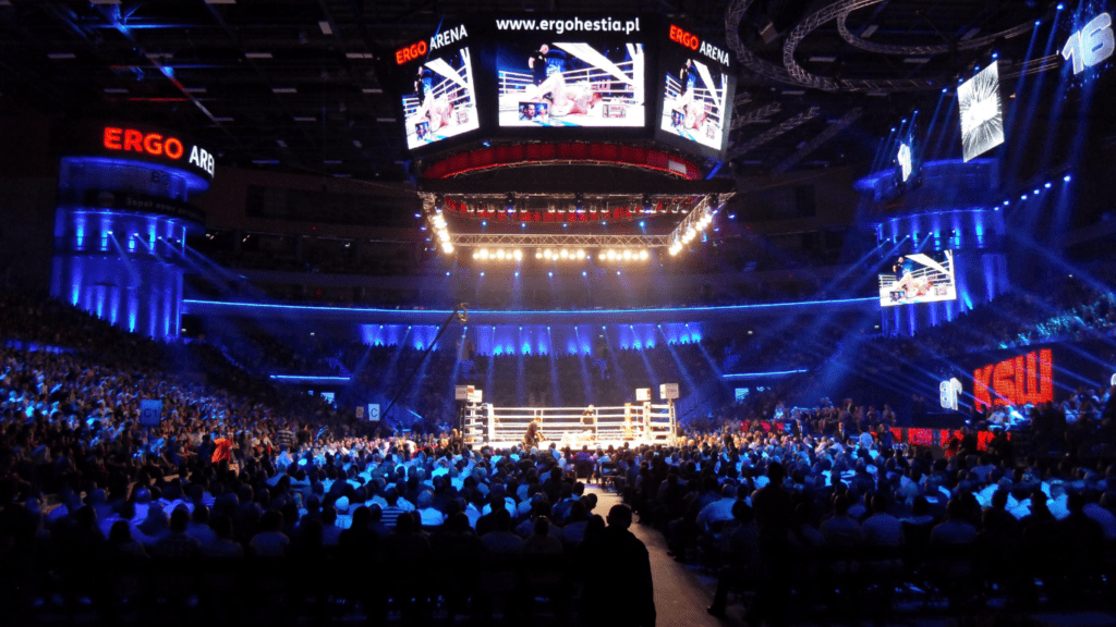 a boxing match is shown on a large screen in an arena